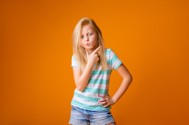 Portrait d'une fille blonde heureuse dans un T-shirt bleu sur un mur jaune