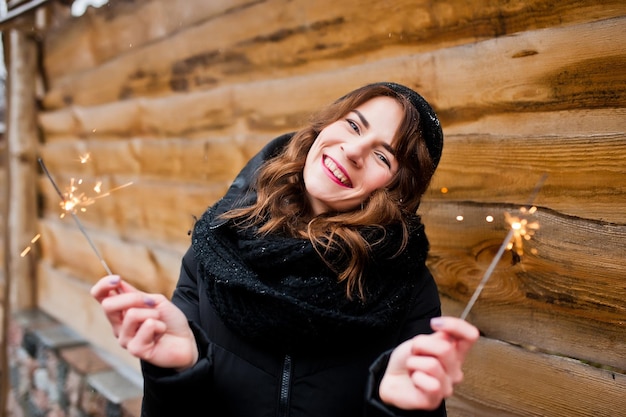 Portrait de fille brune bouclée en veste noire chapeau et écharpe avec feux de bengale à la main