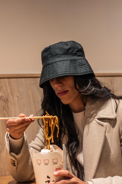 Photo portrait d'une fille brune mangeant des nouilles à emporter dans un bar