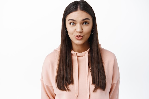 Portrait d'une fille brune surprise et excitée levant les sourcils et souriante étonnée, entendez de bonnes nouvelles, debout contre un mur blanc