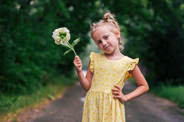 Portrait de fille caucasienne de 6 ans en robe jaune et bottes de pluie debout dans le parc tenant une fleur de pivoine