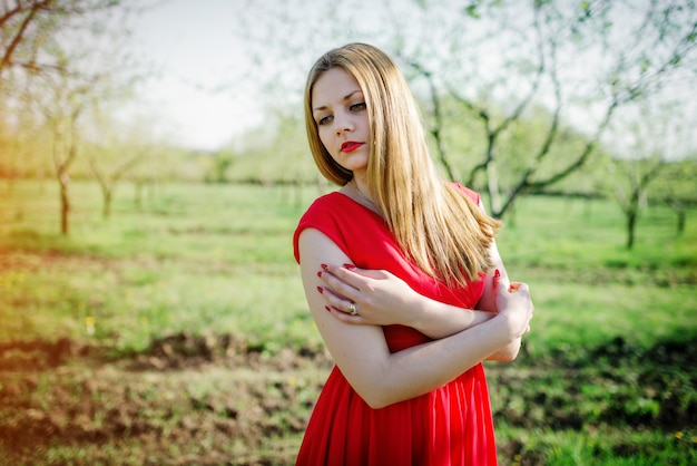 Portrait de fille cheveux clairs sur une robe rouge dans le jardin.