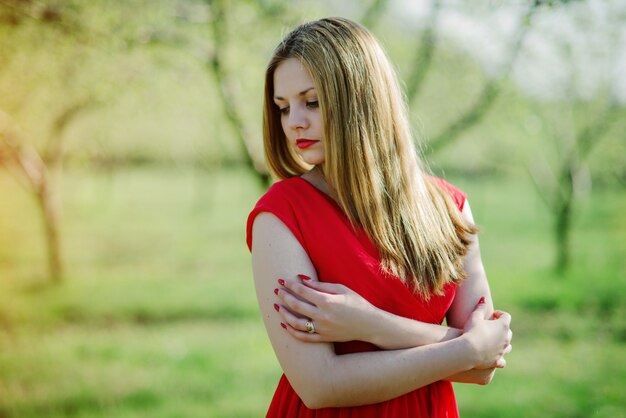 Portrait de fille cheveux clairs sur une robe rouge dans le jardin.