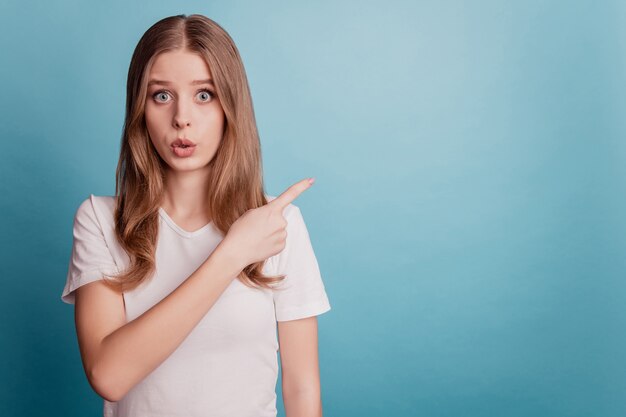 Portrait d'une fille de conseiller sans voix choquée indiquer un espace vide de doigt présentant une nouveauté sur fond bleu