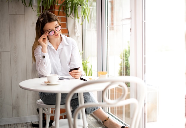 Portrait d'une fille dans un café fait des achats en ligne en payant avec une carte de crédit. Téléphone portable sur la table de la cafétéria et femmes avec une carte de crédit à la main. Cyber café. concept de paiement