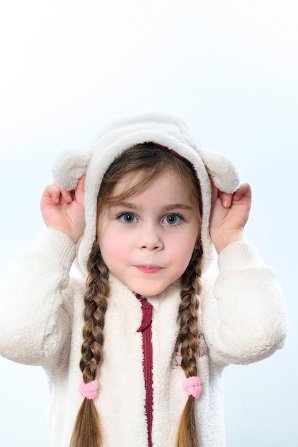 Portrait d'une fille dans un chandail chaud blanc sur fond blanc l'enfant est tressé en deux longues nattes