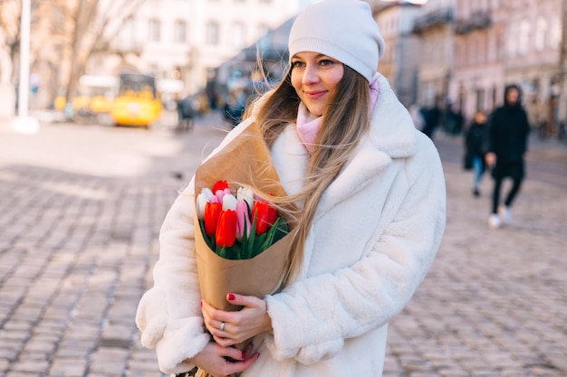 Portrait d'une fille dans un manteau de fourrure et un chapeau avec un bouquet de ville de tulipes colorées