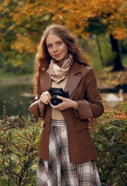 portrait d'une fille dans un parc dans une veste en cuir marron avec un appareil photo