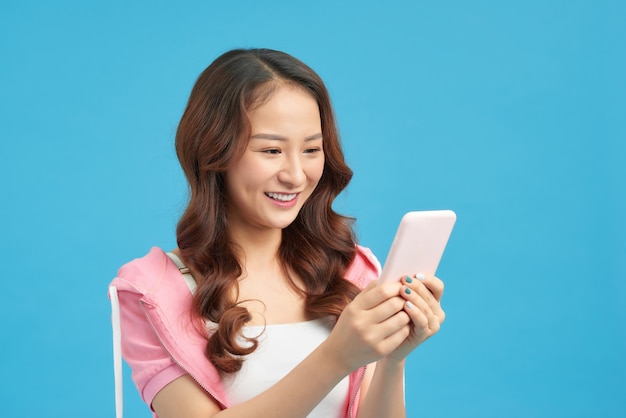 Portrait d'une fille décontractée heureuse regardant un téléphone portable et célébrant isolé sur fond bleu