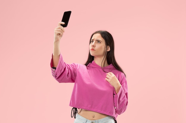 Portrait d'une fille décontractée souriante et confiante faisant une photo de selfie par téléphone portable isolée sur un mur rose.