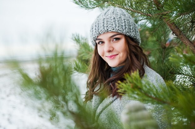 Portrait de fille douce en manteau gris et chapeau contre l'arbre du nouvel an en plein air.