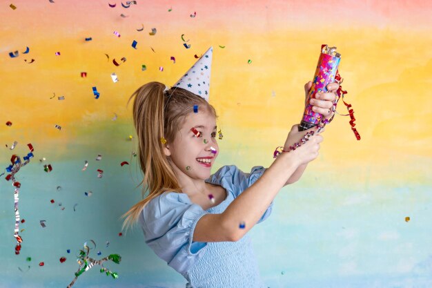 Portrait d'une fille drôle avec un chapeau d'anniversaire et des confettis brillants sur fond jaune