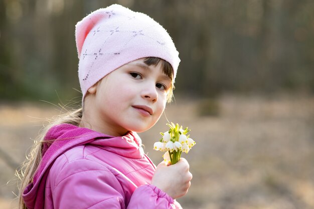 Portrait de fille enfant heureux holding bouquet de fleurs de perce-neige au début du printemps à l'extérieur.