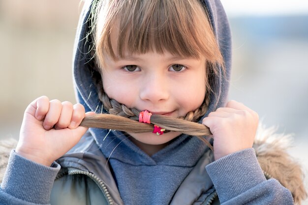 Portrait de fille enfant heureux avec des tresses de cheveux dans des vêtements chauds en automne à l'extérieur.