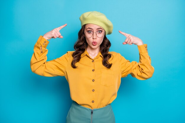 Portrait d'une fille étonnée pointer l'index de sa casquette n'aime pas avoir l'air isolée sur fond de couleur bleu