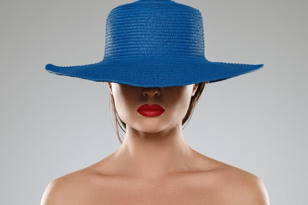 Portrait d'une fille étrangère aux lèvres rouges portant un chapeau bleu sur fond gris