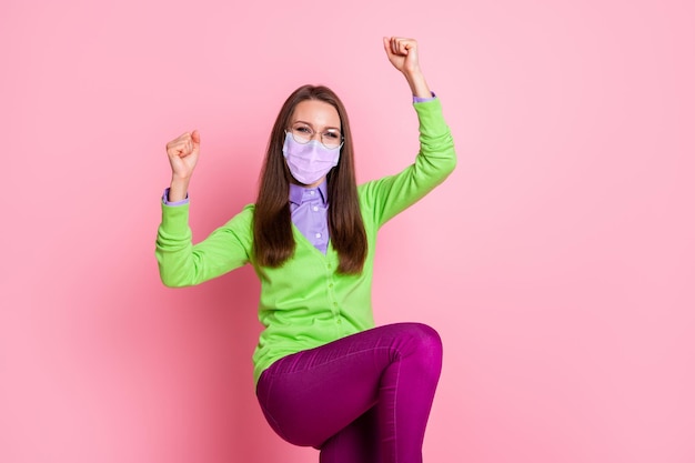 Portrait d'une fille extatique gagner lever les poings porter un masque médical respiratoire isolé sur fond de couleur pastel