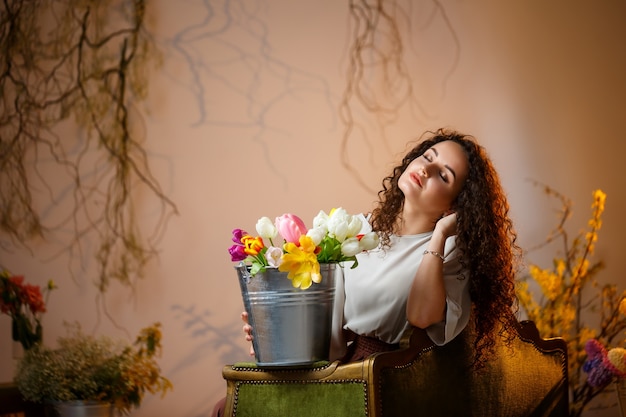 Portrait d'une fille frisée avec un seau de tulipes. Des fleurs fraîches pour de belles photos. Photos délicates avec des fleurs en studio