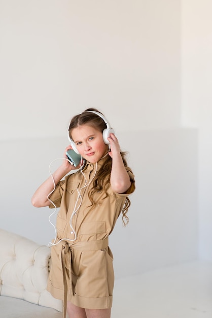 Portrait d'une fille gaie dans une salopette brune élégante écoutant de la musique sur des écouteurs