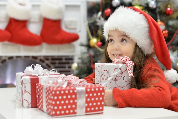 Portrait de fille heureuse en bonnet de Noel assis avec des cadeaux de Noël