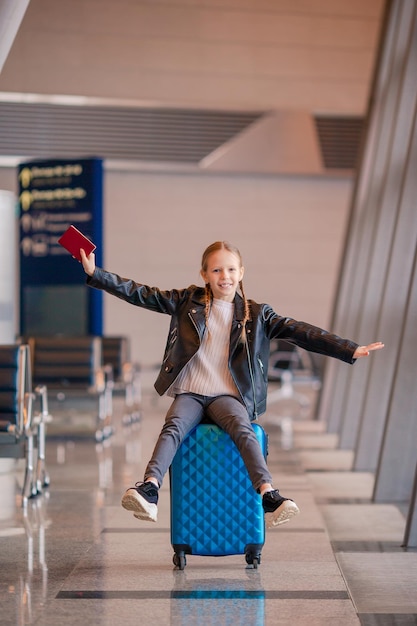 Portrait d'une fille heureuse avec les bras tendus assise sur une valise.