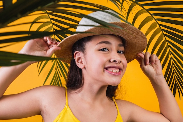 Portrait de fille heureuse avec chapeau et feuilles de palmier sur fond jaune.