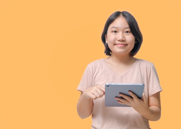 Photo portrait d'une fille heureuse en chemise rose à l'aide d'une tablette isolée sur fond orange