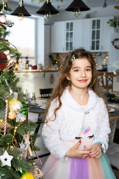 Portrait d'une fille heureuse avec les cheveux longs dans une belle robe dans une maison avec un arbre de Noël