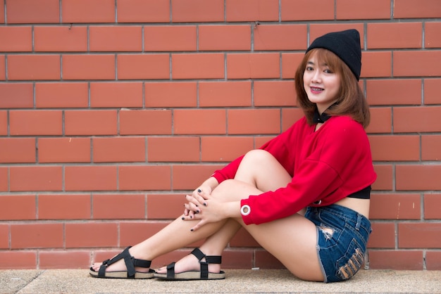 Portrait d'une fille hipster sur fond de mur de briques, belle femme asiatique pose pour prendre une photo, Kawai