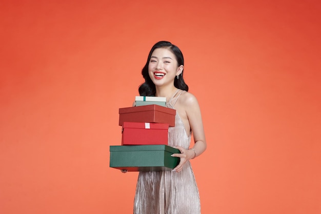 Portrait d'une fille joyeuse vêtue d'une robe tenant une pile de coffrets cadeaux