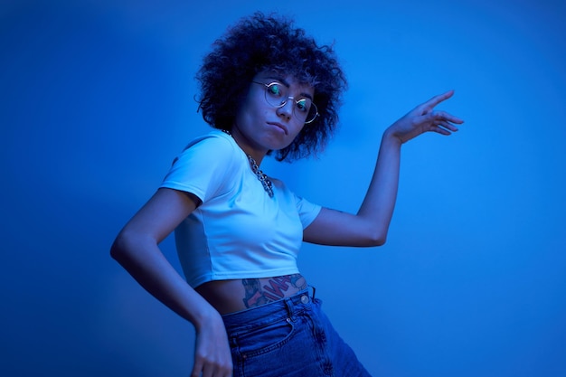 Portrait d'une fille kazakhe cool avec des boucles et un tatouage dansant et posant dans un néon isolé sur fond de studio