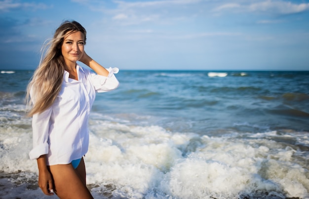 Portrait d'une fille en maillot de bain bleu et chemise blanche sur fond de mer bleue et de ciel clair