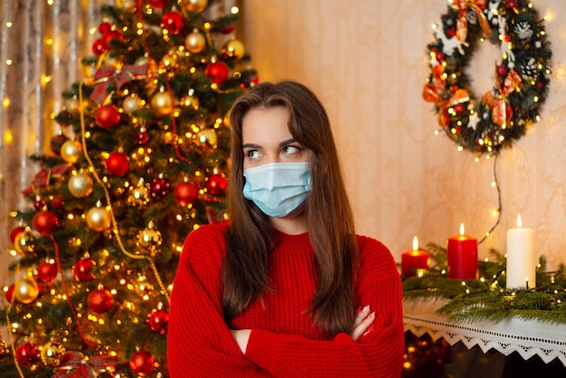 Portrait d'une fille malade et fatiguée de porter des masques médicaux de protection dans une pièce décorée avec un arbre de Noël en arrière-plan Pandémie de coronavirus pendant le concept des vacances de Noël