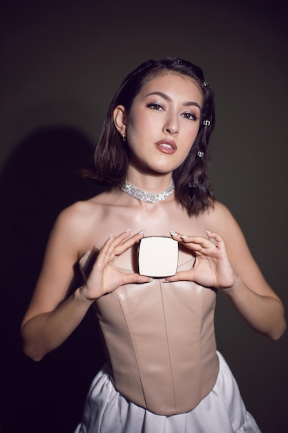 Portrait d'une fille maquilleuse à la mode sexy dans une jupe blanche montre une boîte carrée blanche de poudre debout dans le studio