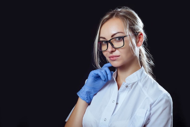 Portrait d'une fille médecin sur fond noir dans des verres pour la vision et des gants