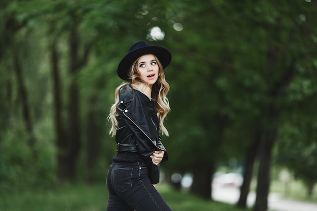 Portrait de fille modèle excitée avec maquillage tendance dans une veste en cuir noire et un chapeau noir posant sur fond vert