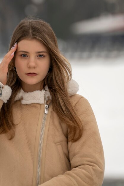 Portrait d'une fille pencive en manteau en peau de mouton beige dans un parc enneigé