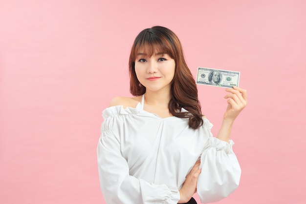 Portrait d'une fille pensive souriante tenant des billets en argent et regardant loin isolé sur fond rose