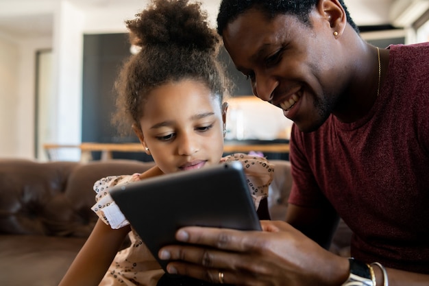 Portrait d'une fille et d'un père s'amusant ensemble et jouant avec une tablette numérique à la maison. Concept monoparental.