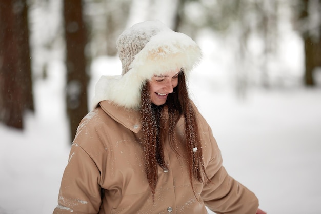 Portrait d'une fille positive heureuse jeune belle femme s'amusant dans la forêt enneigée lors d'une froide journée d'hiver jouant avec la neige profitez d'une journée d'hiver glaciale pendant les vacances d'hiver en jetant de la neige blanche dans l'air