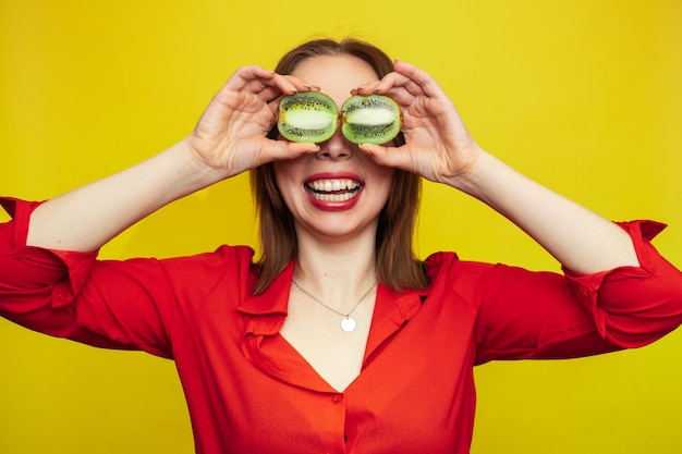 Portrait d'une fille de race blanche avec une peau propre et rayonnante tenant des moitiés de kiwi isolées sur fond jaune Le concept de cosmétiques avec des vitamines