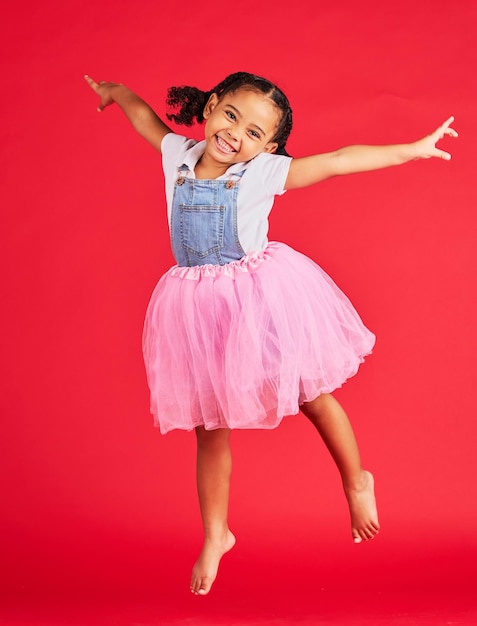 Portrait fille et sauter en jupe tutu sur fond rouge studio et mode amusante Vêtements de ballet enfant heureux et énergie pour la danse de performance et sourire avec bonheur robe de ballerine et princesse