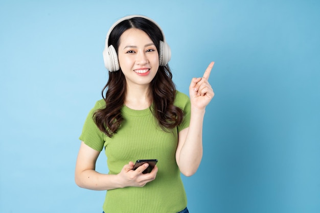 Portrait de fille sauterelle asiatique écoute de la musique, isolé sur fond bleu