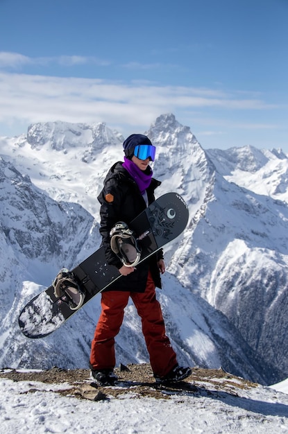 Portrait d'une fille avec snowboard au sommet d'une montagne enneigée.