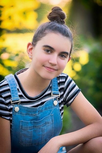 Photo portrait d'une fille souriante assise contre des arbres dans un parc