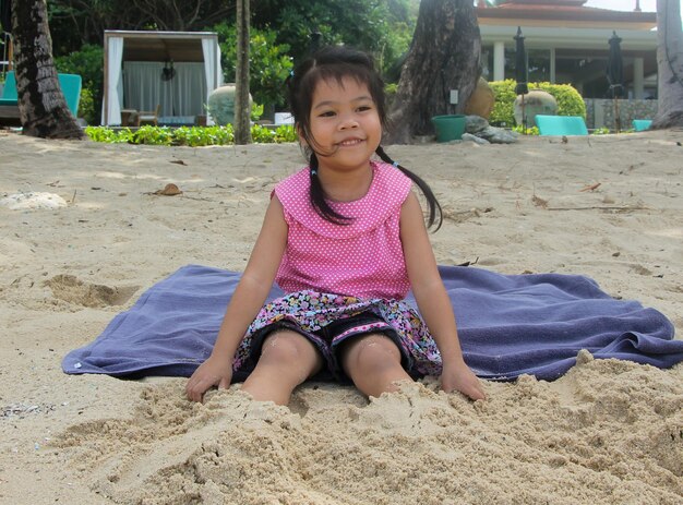 Portrait d'une fille souriante assise sur le sable