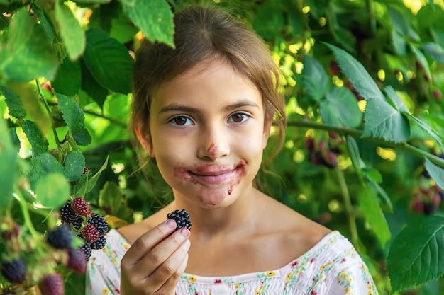 Photo portrait d'une fille souriante mangeant des framboises noires