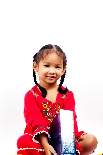 Photo portrait d'une fille souriante tenant un cadeau de noël alors qu'elle est assise sur un fond blanc