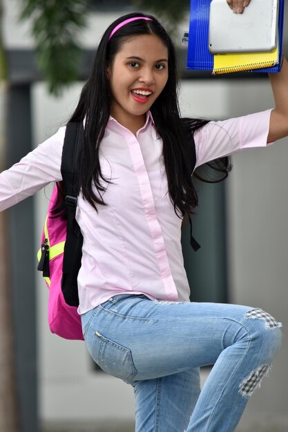 Photo portrait d'une fille souriante tenant un livre et une tablette numérique debout sur une jambe