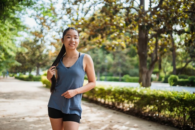 Portrait d'une fille sportive souriante asiatique regardant la caméra pendant qu'elle touche ses cheveux